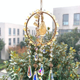 Sonnenfänger Rohstein Citrin mit goldenem Ring und langen Kristallprismen, aufgehängt vor dem Fenster im Sonnenlicht