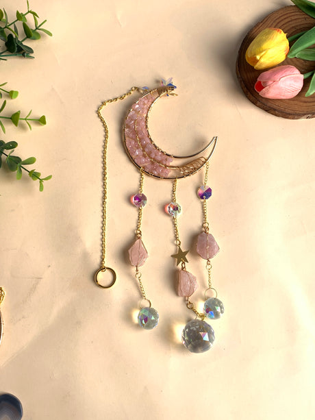 Handgefertigter Mond-Sonnenfänger mit Rosenquarz-Chips, goldfarbenem Rahmen und vier Strängen, bestückt mit rohen Rosenquarz-Anhängern und facettierten Lichtkristallkugeln.