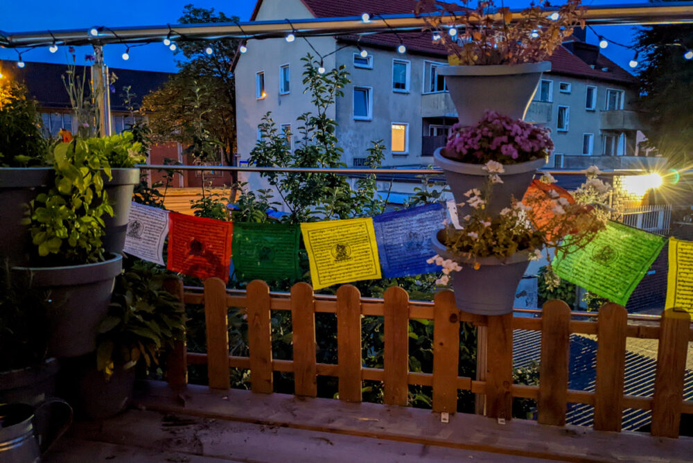 Stimmungsvoller Balkon am Abend mit Blumen, Lichterketten und Gebetsfahne